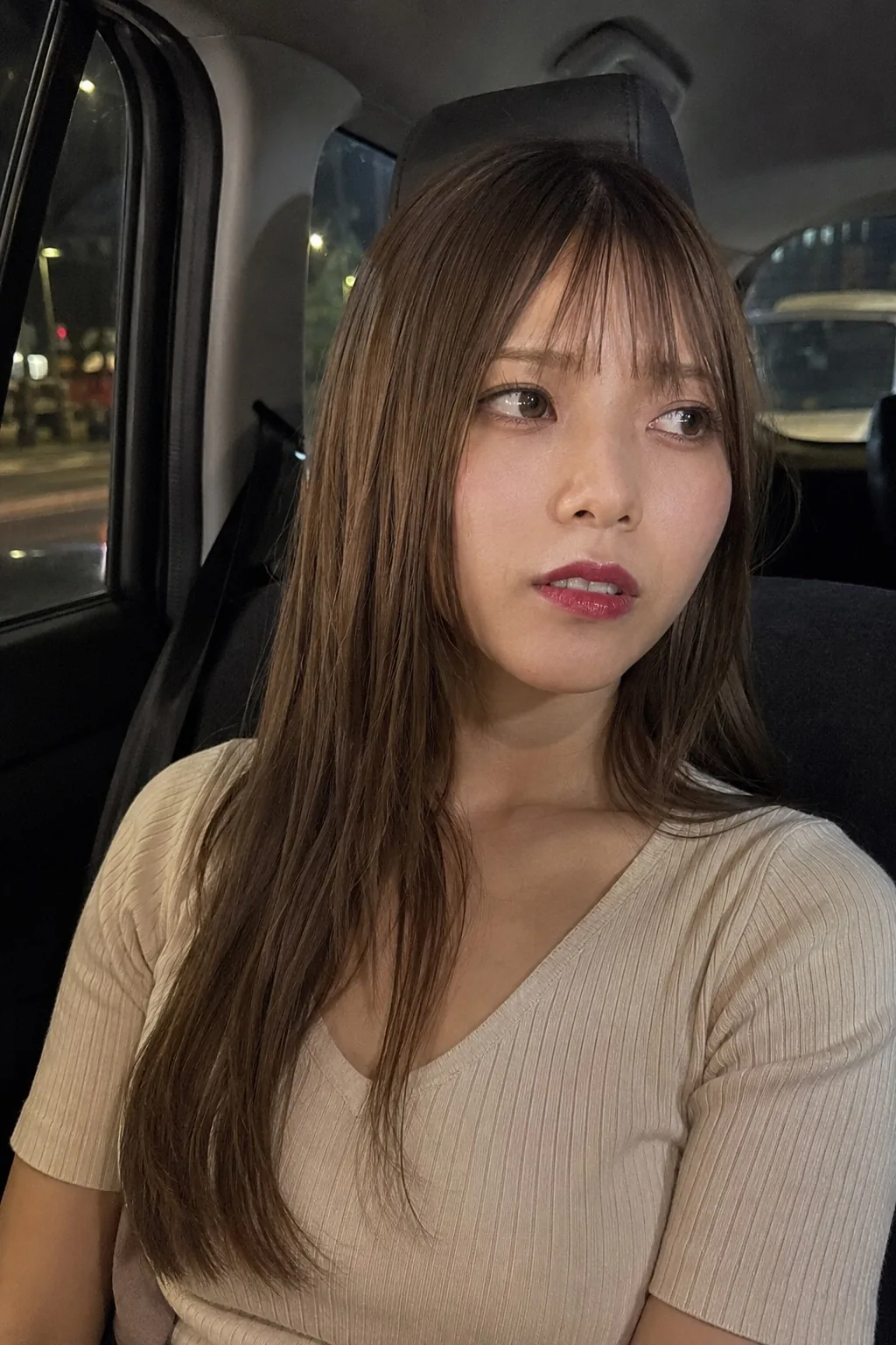 夜の車内でクリーム色の半袖トップスを着て横を見る人物